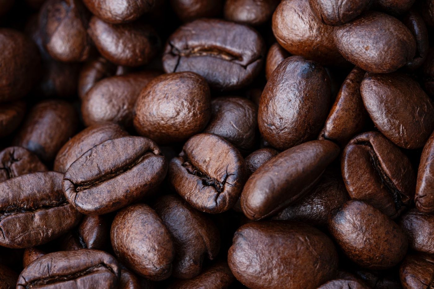 A close macro photograph of roasted coffee beans filling the frame, showing the range of browns within a single batch.